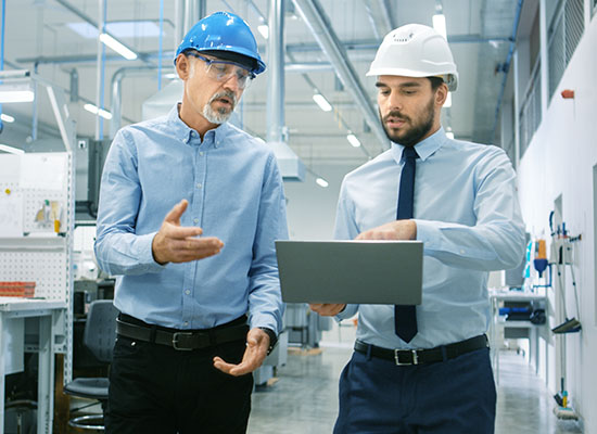 Two men in hardhats with suits on looking at laptop