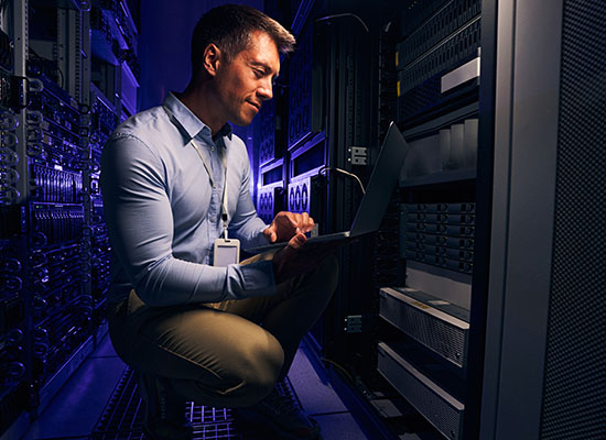 Man crouching looking at laptop in computer server room
