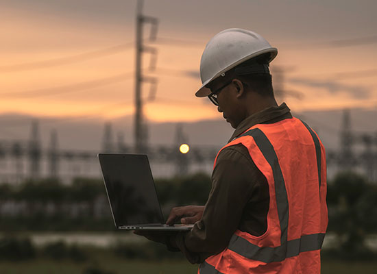 Man in safety vest with hardhat looking at laptop
