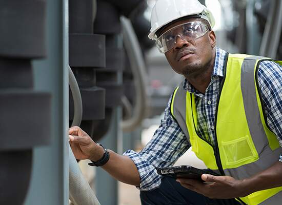 Man in safety vest and hardhat looking at machine while holding a tablet