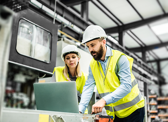 Man and women in safety vests and hard hats looking at laptop